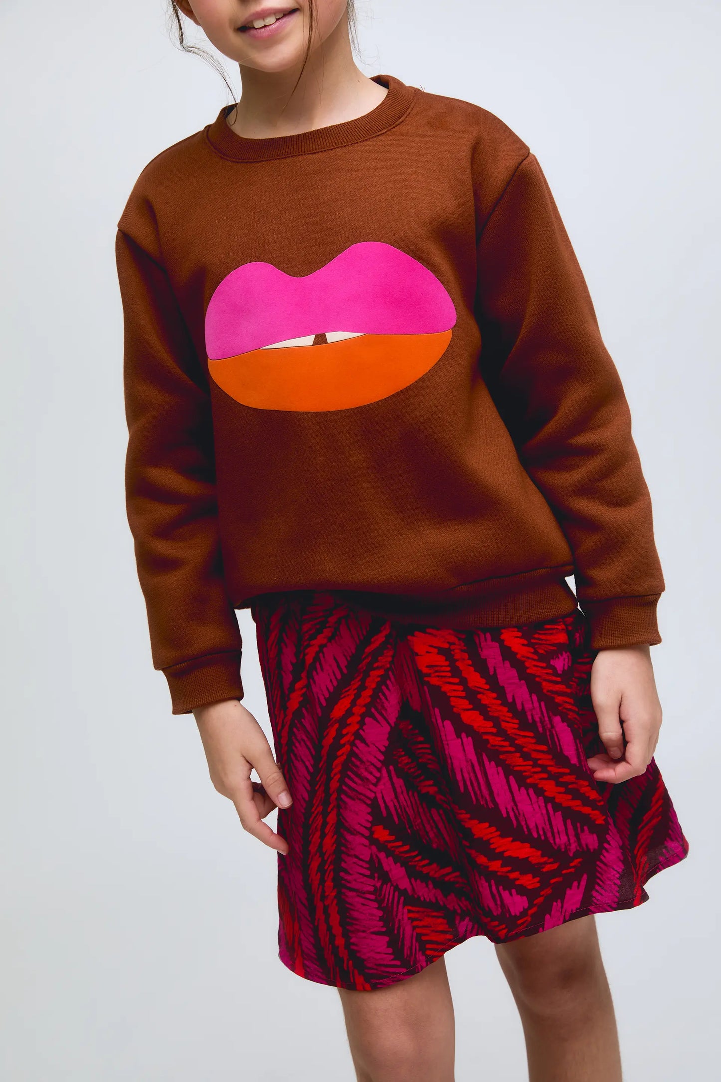 Sudadera de niña marrón con estampado de labios en fucsia y naranja.